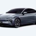 Sleek Dongfeng eπ 007 electric sedan in Night Shadow Black, showcasing its aerodynamic fastback design, split LED headlights with 104 LEDs, and optional electric scissor doors, parked against a modern city backdrop.