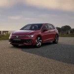 A red Volkswagen Golf GTI Mk 8.5 parked on a city street, showcasing its sporty exterior with matrix LED headlights, a honeycomb front bumper, red GTI badges, and 18-inch Richmond alloy wheels. The sleek five-door hatchback features a dynamic stance with a rear diffuser, twin chrome exhaust tips, and smoked LED taillights.