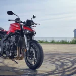 Side view of the 2025 Honda CB1000 Hornet SP in Matte Ballistic Black Metallic with gold accents, showcasing its aggressive streetfighter design, LED headlight, and chiselled 17-litre fuel tank, parked on an urban street in India.
